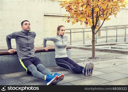 fitness, sport, exercising, training and people concept - couple doing triceps dip exercise on city street bench. couple doing triceps dip on city street bench