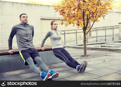fitness, sport, exercising, training and people concept - couple doing triceps dip exercise on city street bench. couple doing triceps dip on city street bench