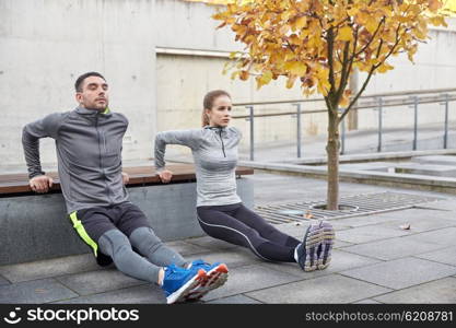 fitness, sport, exercising, training and people concept - couple doing triceps dip exercise on city street bench