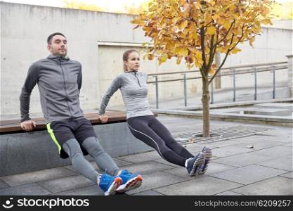 fitness, sport, exercising, training and people concept - couple doing triceps dip exercise on city street bench