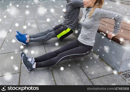 fitness, sport, exercising, training and people concept - couple of sportsmen doing triceps dip exercise on city street bench over snow
