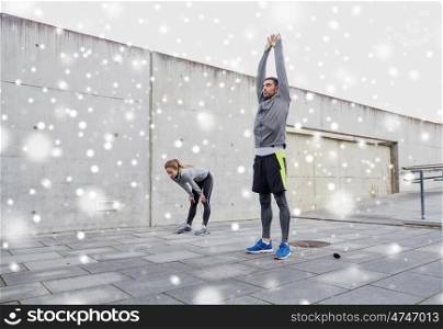 fitness, sport, exercising, training and people concept - tired couple of sportsmen with jumping ropes stretching after exercise outdoors on city street over snow