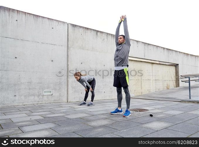 fitness, sport, exercising, training and people concept - tired couple stretching after exercise outdoors on city street