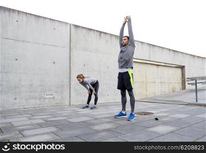 fitness, sport, exercising, training and people concept - tired couple stretching after exercise outdoors on city street