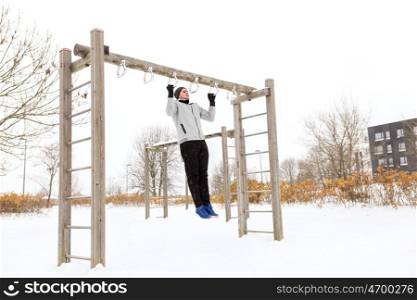fitness, sport, exercising, training and people concept - young man doing pull ups on horizontal bar outdoors in winter