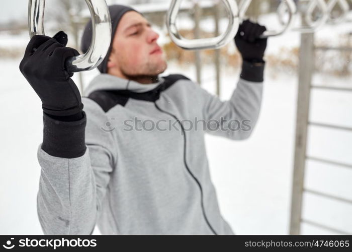 fitness, sport, exercising, training and people concept - young man doing pull ups on horizontal bar outdoors in winter