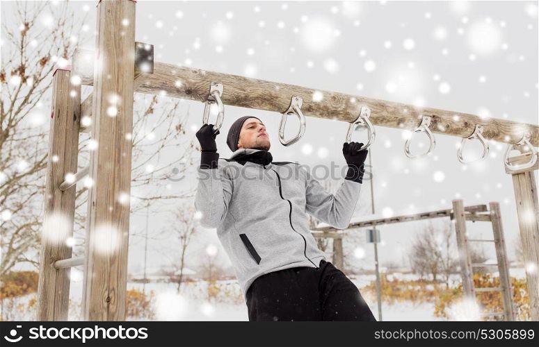 fitness, sport, exercising, training and people concept - young man doing pull ups on horizontal bar outdoors in winter. young man exercising on horizontal bar in winter