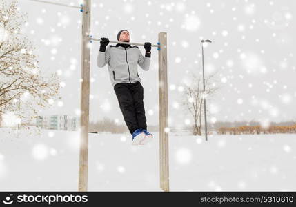 fitness, sport, exercising, training and people concept - young man doing pull ups on horizontal bar outdoors in winter. young man exercising on horizontal bar in winter