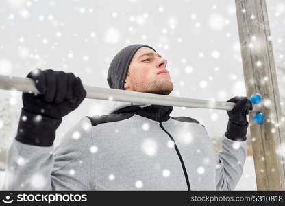 fitness, sport, exercising, training and people concept - young man doing pull ups on horizontal bar outdoors in winter. young man exercising on horizontal bar in winter