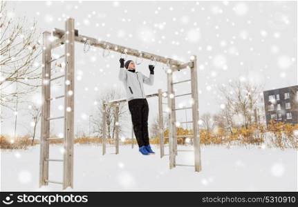 fitness, sport, exercising, training and people concept - young man doing pull ups on horizontal bar outdoors in winter. young man exercising on horizontal bar in winter