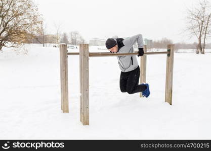 fitness, sport, exercising, training and people concept - young man doing triceps dip on parallel bars outdoors in winter