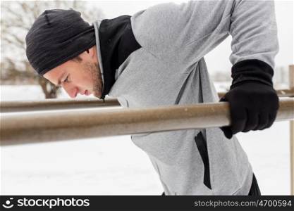 fitness, sport, exercising, training and people concept - young man doing triceps dip on parallel bars outdoors in winter