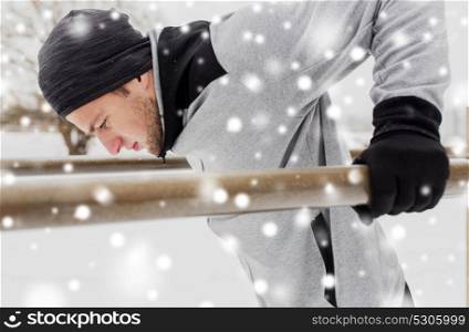 fitness, sport, exercising, training and people concept - young man doing triceps dip on parallel bars outdoors in winter. young man exercising on parallel bars in winter