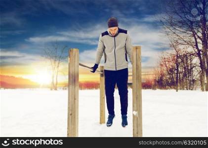 fitness, sport, exercising, training and people concept - young man doing triceps dip on parallel bars outdoors in winter. young man exercising on parallel bars in winter