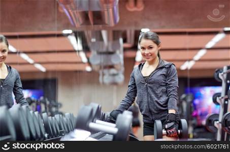 fitness, sport, exercising, weightlifting and people concept - smiling young woman choosing dumbbells in gym