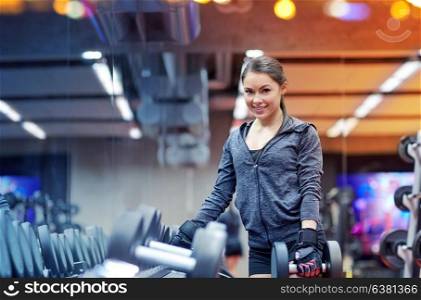 fitness, sport, exercising, weightlifting and people concept - smiling young woman choosing dumbbells in gym. smiling young woman choosing dumbbells in gym