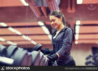 fitness, sport, exercising, weightlifting and people concept - young smiling woman choosing dumbbells in gym. young smiling woman choosing dumbbells in gym