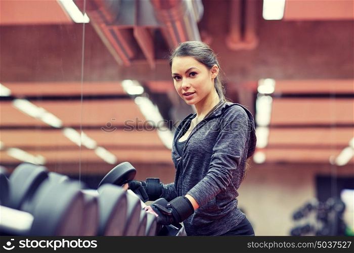 fitness, sport, exercising, weightlifting and people concept - young woman choosing dumbbells in gym. young woman choosing dumbbells in gym