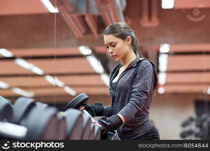 fitness, sport, exercising, weightlifting and people concept - young woman choosing dumbbells in gym