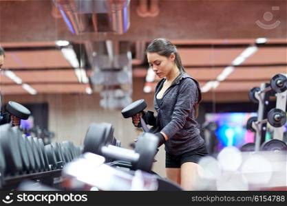 fitness, sport, exercising, weightlifting and people concept - young woman choosing dumbbells in gym