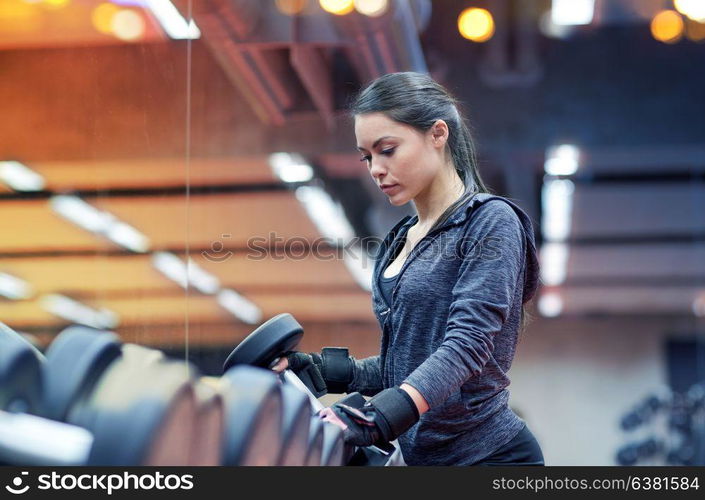 fitness, sport, exercising, weightlifting and people concept - young woman choosing dumbbells in gym. young woman choosing dumbbells in gym