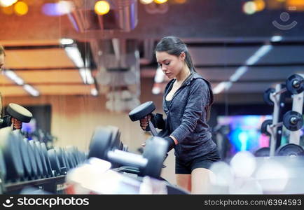 fitness, sport, exercising, weightlifting and people concept - young woman choosing dumbbells in gym. young woman choosing dumbbells in gym