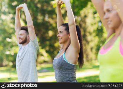 fitness, sport, friendship and healthy lifestyle concept - group of happy teenage friends or sportsmen exercising and stretching hands up at boot camp