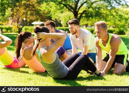 fitness, sport, friendship and healthy lifestyle concept - group of happy teenage friends or sportsmen exercising and doing sit-ups at boot camp