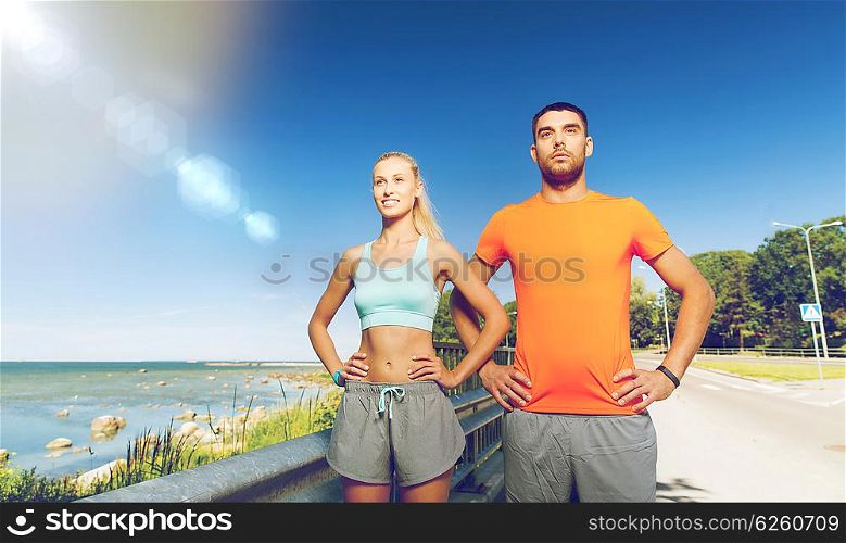 fitness, sport, friendship and healthy lifestyle concept - happy couple exercising at summer seaside