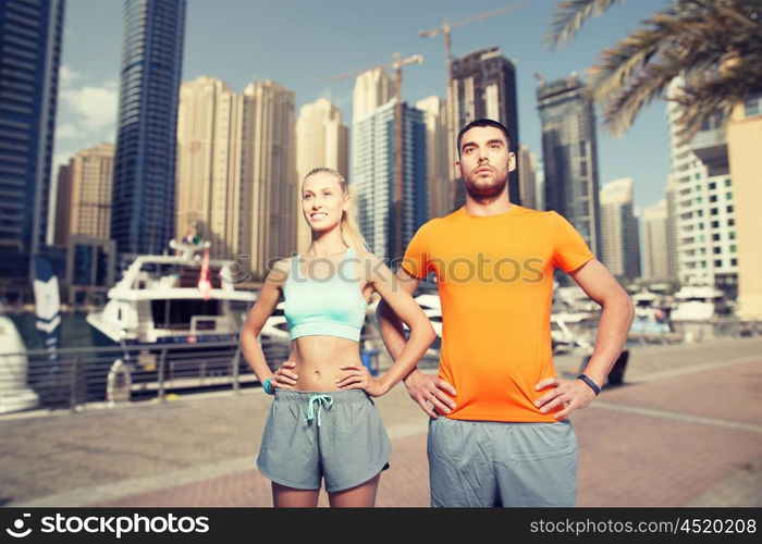 fitness, sport, friendship and healthy lifestyle concept - happy couple exercising over dubai city street background