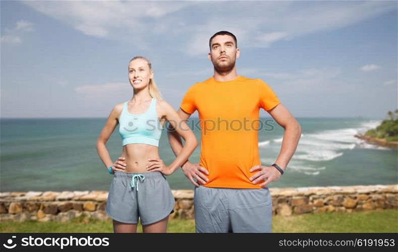 fitness, sport, friendship and healthy lifestyle concept - happy couple exercising over sea or beach background