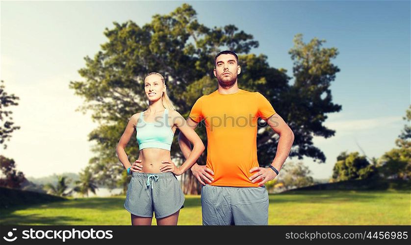 fitness, sport, friendship and healthy lifestyle concept - happy couple exercising over summer park background
