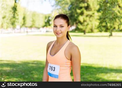 fitness, sport, friendship and healthy lifestyle concept - happy young woman at running marathon with badge number in summer park. woman at running marathon with badge number