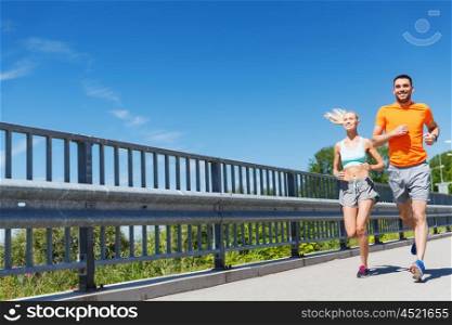 fitness, sport, friendship and healthy lifestyle concept - smiling couple running at summer seaside