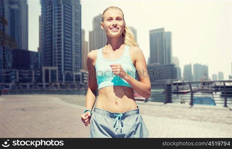 fitness, sport, friendship and healthy lifestyle concept - smiling young woman running or jogging over dubai city street background