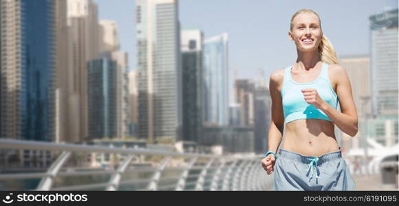 fitness, sport, friendship and healthy lifestyle concept - smiling young woman running or jogging over dubai city street background