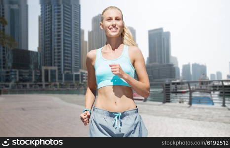 fitness, sport, friendship and healthy lifestyle concept - smiling young woman running or jogging over dubai city street background