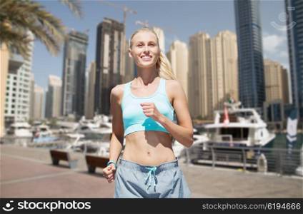 fitness, sport, friendship and healthy lifestyle concept - smiling young woman running or jogging over dubai city street background