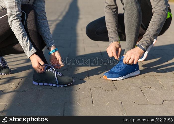 fitness, sport, friendship and lifestyle concept - close up of couple tying shoelaces outdoors