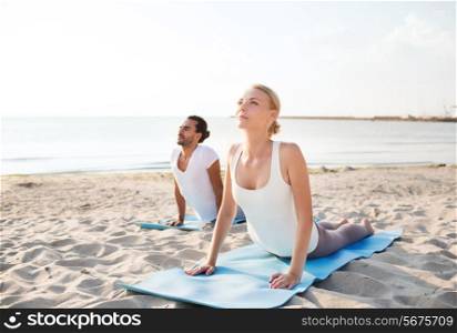 fitness, sport, friendship and lifestyle concept - couple making yoga exercises lying on mats outdoors