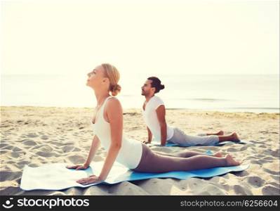 fitness, sport, friendship and lifestyle concept - couple making yoga exercises lying on mats outdoors