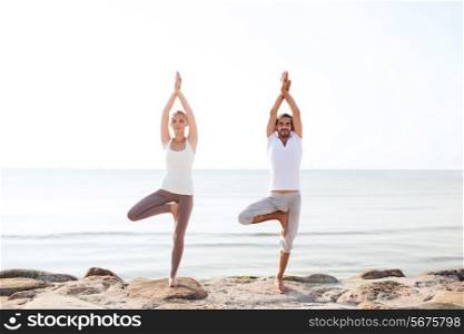 fitness, sport, friendship and lifestyle concept - couple making yoga exercises on beach