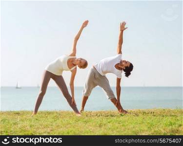 fitness, sport, friendship and lifestyle concept - couple making yoga exercises outdoors