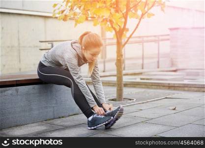 fitness, sport, friendship and lifestyle concept - happy young sporty woman tying shoelaces outdoors