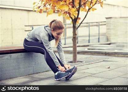 fitness, sport, friendship and lifestyle concept - happy young sporty woman tying shoelaces outdoors. happy young sporty woman tying shoelaces outdoors