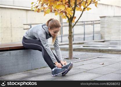 fitness, sport, friendship and lifestyle concept - happy young sporty woman tying shoelaces outdoors