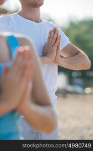 Fitness, sport, friendship and lifestyle concept - smiling couple making meditation yoga exercises on beach at morning