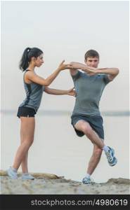 Fitness, sport, friendship and lifestyle concept - smiling couple making stretching yoga exercises on beach at morning