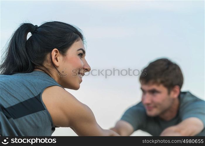 Fitness, sport, friendship and lifestyle concept - smiling couple making stretching yoga exercises on beach at morning