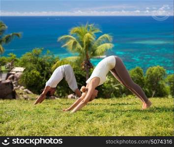 fitness, sport, friendship and lifestyle concept - smiling couple making yoga exercises outdoors over natural background and sea. smiling couple making yoga exercises outdoors